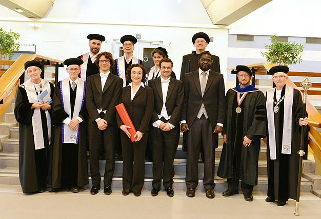 Group of academics in formal robes and doctoral caps posed on a staircase.
