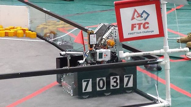 Team 7037's robot on the FTC competition field, with the FIRST Tech Challenge banner overhead.