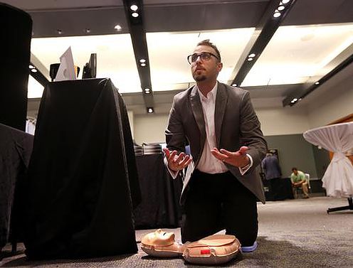 Justin Maestri kneeling beside a training mannequin, demonstrating AIMS at the MODSIM World Conference & Expo.
