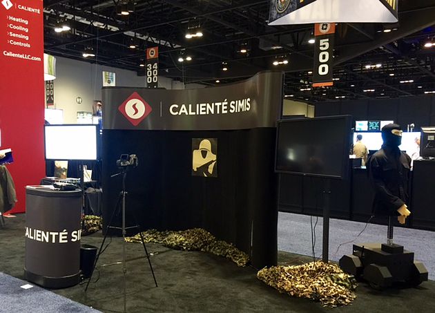 Caliente SimIS trade show booth featuring a camouflaged robotic target and mannequin display.