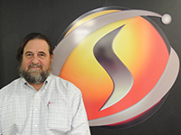 Warren Bizub, SimIS Chief Technology Officer, standing in front of the SimIS logo.