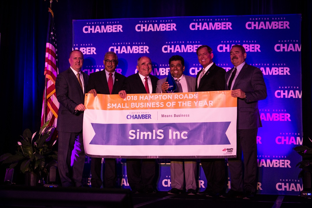 Dr. Johnny Garcia and other officials holding a '2018 Hampton Roads Small Business of the Year, SimIS Inc' banner at the Chamber ceremony.