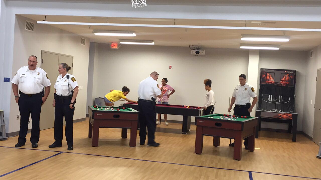 Portsmouth PD officers watch children playing pool at the PAL Summer Camp recreation room.