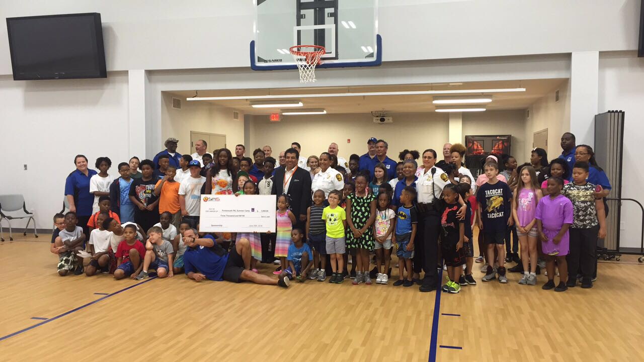 Dr. Johnny Garcia and Portsmouth PD officers present a $3,000 sponsorship check to PAL Summer Camp children in the gymnasium.