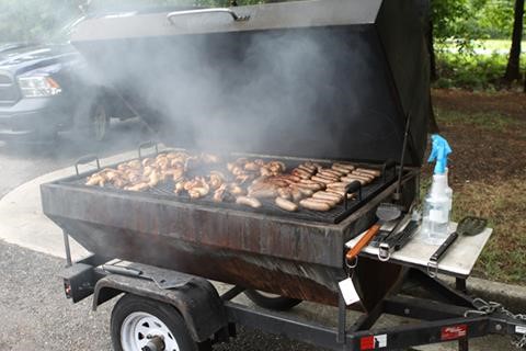 Chicken and sausages grilling on a large trailer-mounted smoker at the JT&E-Suffolk cookout.