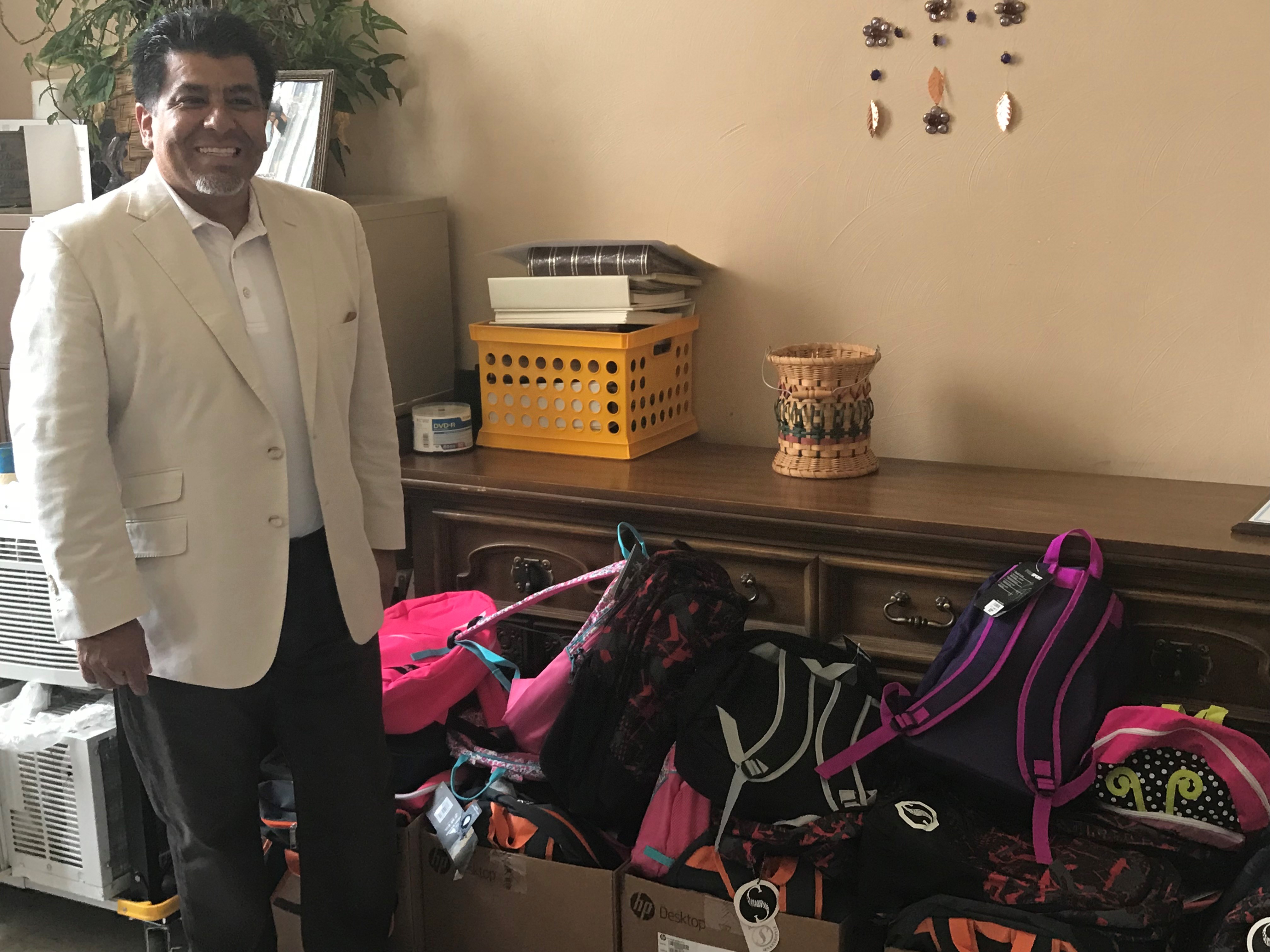 Dr. Johnny Garcia standing beside boxes of donated backpacks at the Wesley Community Center.