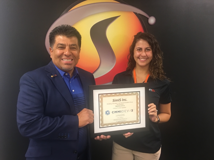 Dr. Johnny Garcia and a SimIS employee holding the framed CMMI Level 3 Development certificate in front of the SimIS logo.