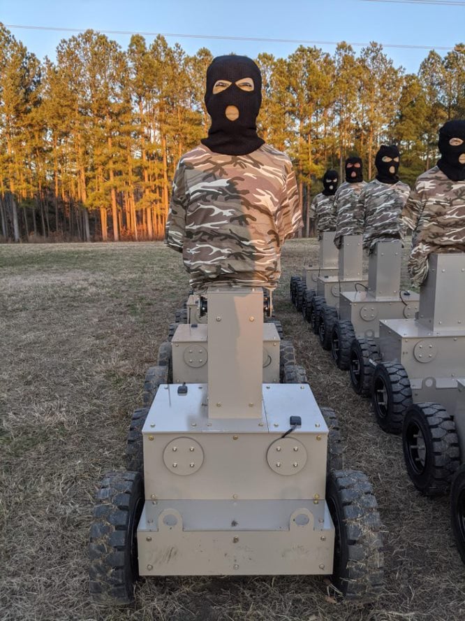 A Human Type Target robot in the foreground, wearing a camouflage shirt and balaclava-style head, with additional robots lined up behind it.