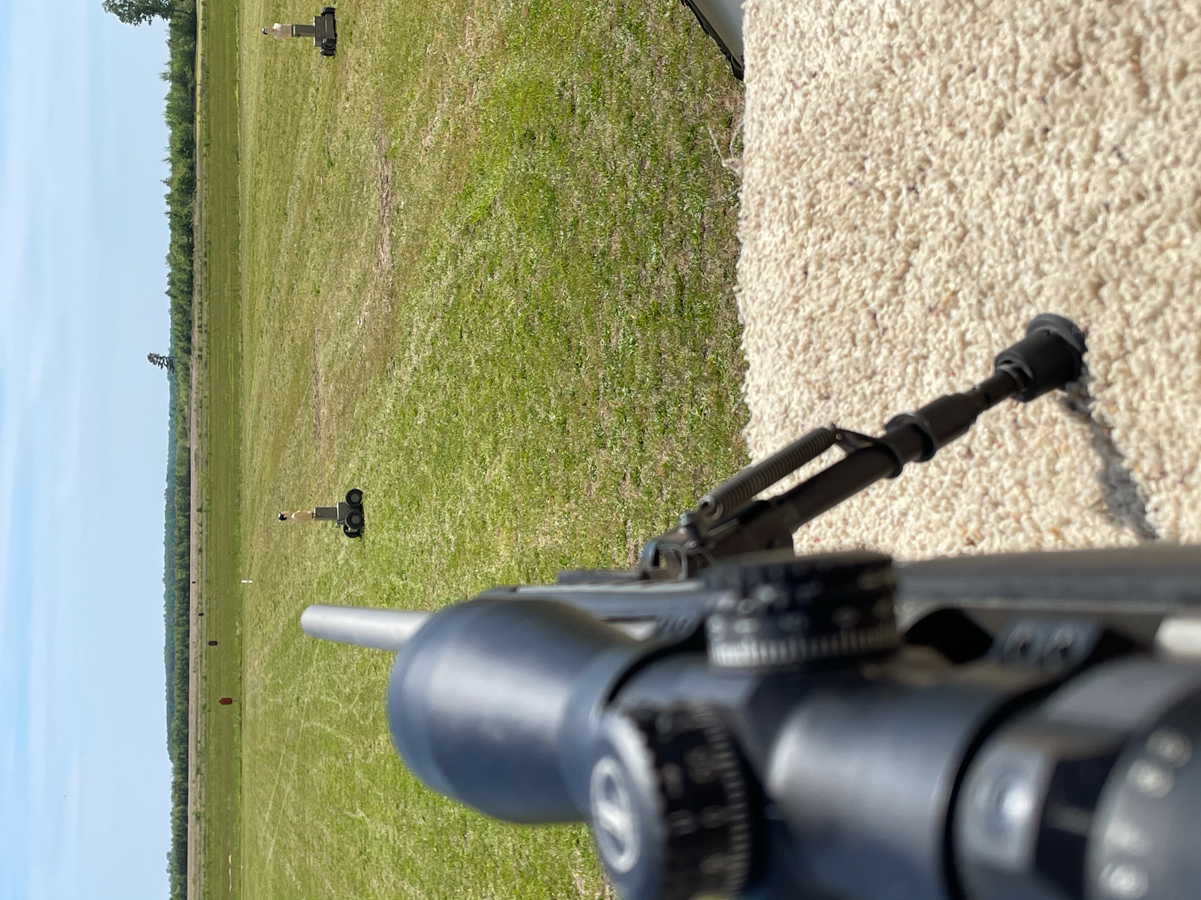 View down a rifle scope toward HTT targets positioned across an open field for long-range training.