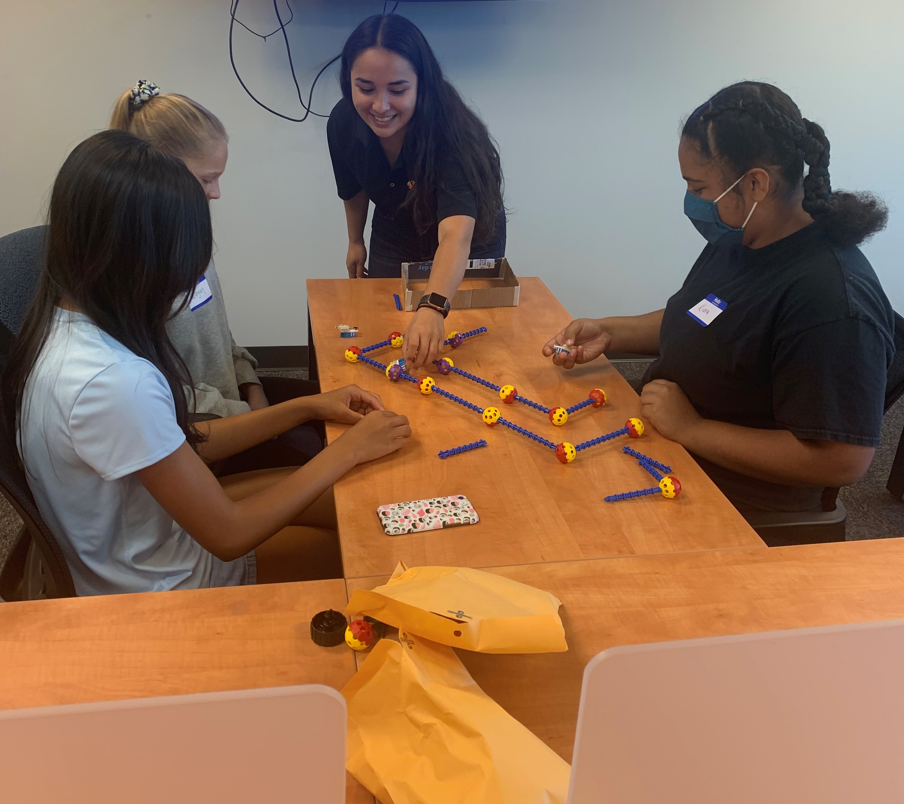 SimIS staff member helping a group of students build a mini bot with colorful ball-and-rod construction pieces at the STEM Kids Camp.