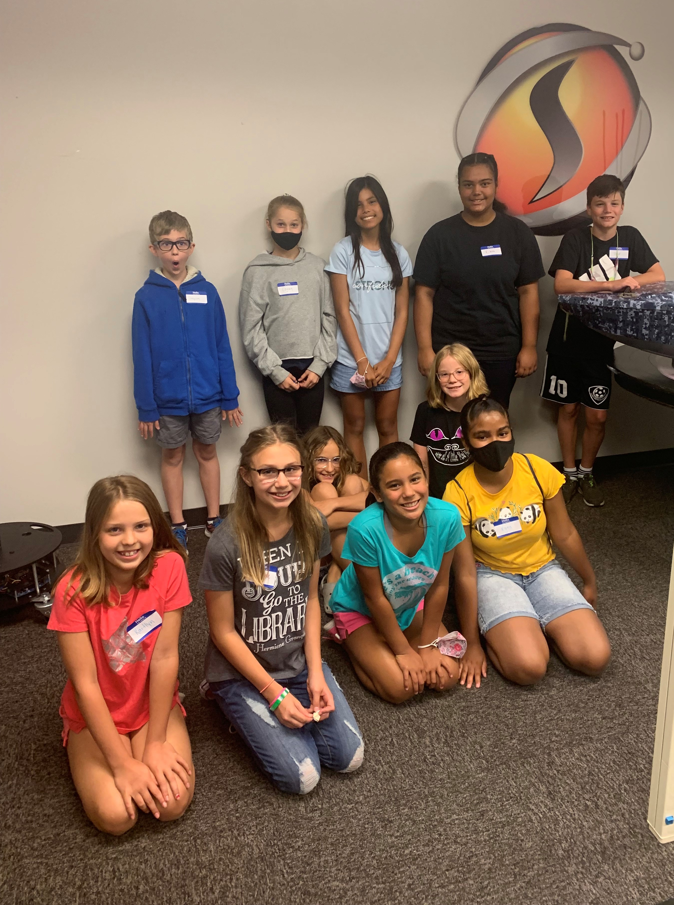 Group photo of STEM Kids Camp participants posing together in front of the SimIS logo.