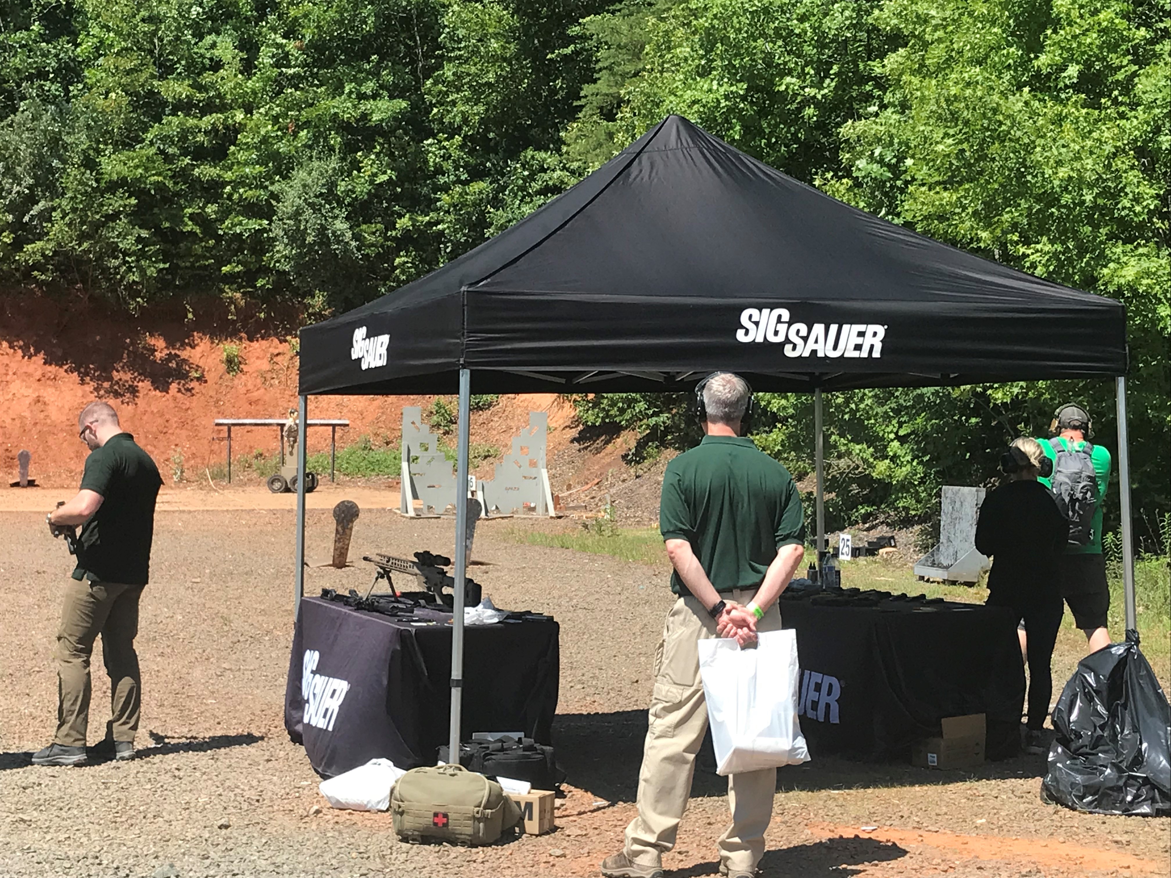 Attendees at the outdoor shooting range under a Sig Sauer tent at the TSSi expo, with the HTT target visible in the background.