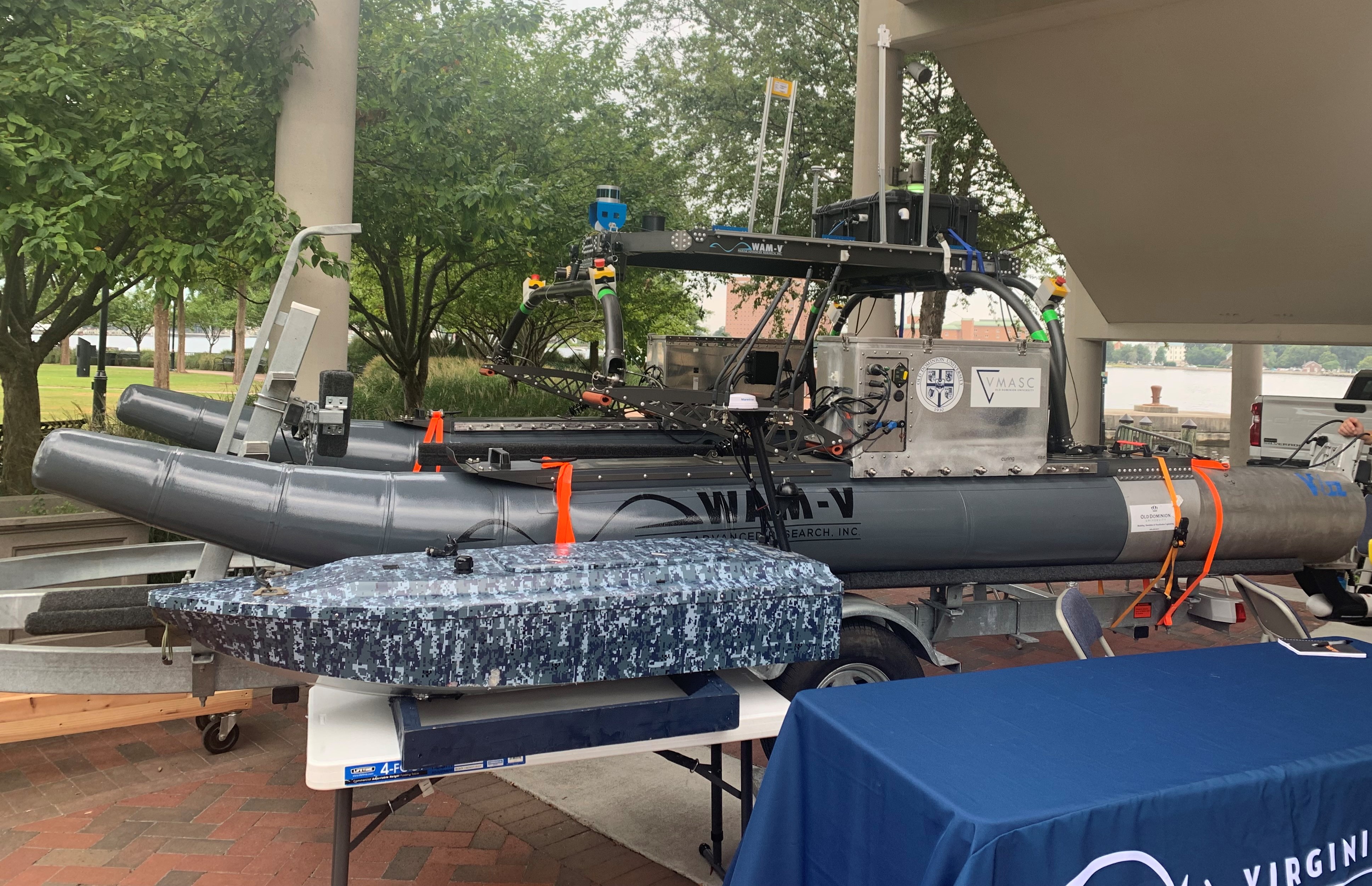 An ODU VMASC unmanned surface vessel and a camouflage-patterned autonomous watercraft on display at the summit.